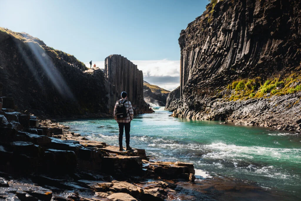 A visitor beside the river and basalt columns in Stuðlagil Canyon